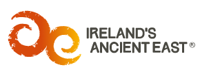 Logo of Ireland's Ancient East; features stylized orange spirals resembling ancient Celtic symbols next to the text "Ireland's Ancient East" in a grey serif font, ideal for incorporation into an SEO