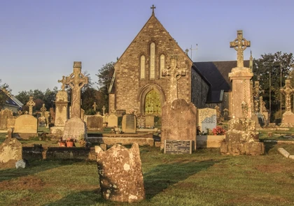 Dunhill Old Church stands proudly amidst an ancient graveyard adorned with weathered headstones and Celtic crosses. Bathed in warm, golden light under a clear blue sky, this historic site is a captivating gem along the Copper Coast.