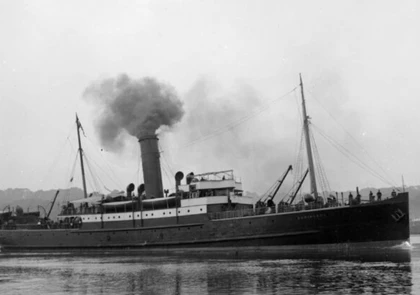 A vintage black and white photograph of a steamship sailing on calm waters near the Copper Coast. Smoke billows from its single large smokestack, capturing a moment before becoming one of the many shipwrecks in the area. The vessel boasts a classic design, with lifeboats and a few people on deck.